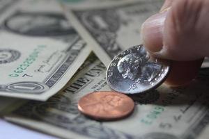 Man's hand picking up a quarter coin from a pile of banknotes and coins. photo