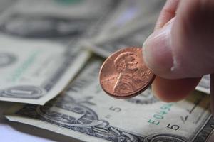 Man's hand picking up penny or cent coin from a pile of banknotes and coins. photo