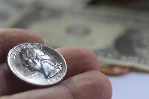 la mano del hombre recogiendo un cuarto de moneda de un montón de billetes y monedas. foto