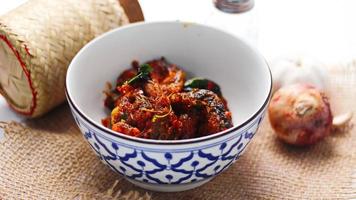 Spicy Stir Fried Catfish served in a Thai style patterned bowl on a white table. photo