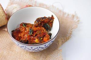 Spicy Stir Fried Catfish served in a Thai style patterned bowl on a white table. photo