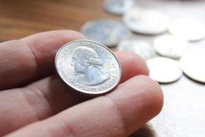 mano recogiendo un cuarto de moneda en moneda americana esparcida en el suelo de madera foto