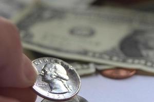 Man's hand picking up a quarter coin from a pile of banknotes and coins. photo