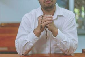 un joven asiático fiel manos en gesto de oración sentado solo en el sofá en la iglesia y rezar. foto