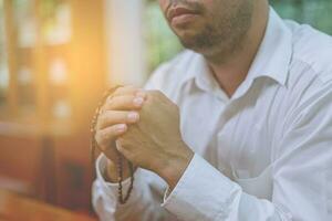 hombre asiático rezando en una iglesia cristiana. man pra,manos dobladas en oración sobre una santa biblia en la iglesia concepto de fe, espiritualidad foto