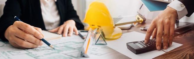 Two colleagues discussing data working and tablet, laptop with on on architectural project at construction site at desk in office photo