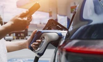 enchufar a mano un cargador en un enchufe de coche eléctrico.coche eléctrico o ev se está cargando en la estación foto