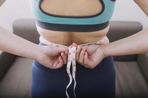 hermosa mujer gorda con cinta métrica usa su mano para exprimir el exceso de grasa que está aislado en un fondo blanco. ella quiere perder peso, el concepto de cirugía y descomponer grasa bajo el foto