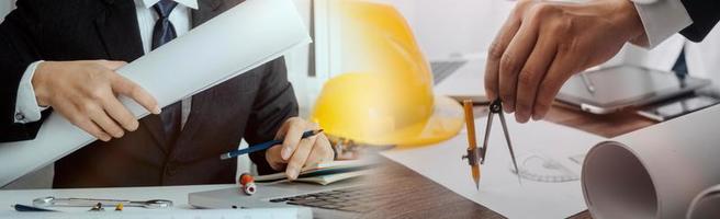 Two colleagues discussing data working and tablet, laptop with on on architectural project at construction site at desk in office photo