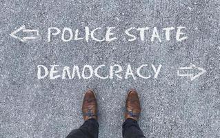 Top view on a man standing in front of the words Police State and Democracy with arrows pointing to the left and right side of the picture photo