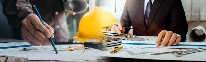 Two colleagues discussing data working and tablet, laptop with on on architectural project at construction site at desk in office photo