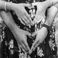 Indian couple posing for maternity baby shoot. The couple is posing in a lawn with green grass and the woman is falunting her baby bump in Lodhi Garden in New Delhi, India - Black and White photo