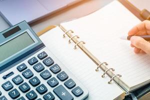 Woman writing on blank planner book with a calculator on side in business concept. photo