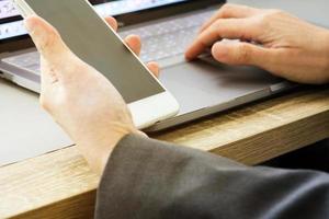 Business woman using mobile phone with left hand and touching touch pad of notebook with right hand photo