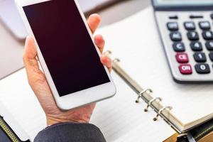 mujer de negocios sosteniendo un teléfono móvil en la mano izquierda con una página en blanco, un libro de planificación de líneas y una calculadora en el concepto de negocio. foto