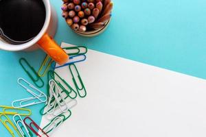 Desktop design with orange mug of coffee, colorful paperclips and colored pencils photo