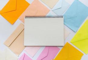 Envelopes in pastel colors align in oblique style with a blank white sketchbook photo