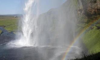 un arco iris frente a la cascada seljalandsfoss en la costa sur de islandia en un día soleado foto