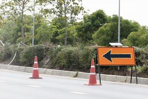 Orange traffic sign with arrow icon  and signal cones on highway photo