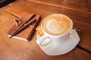 A cup of hot coffee with latte art on the surface placed in the wooden table. photo