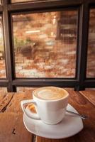 A cup of hot coffee with latte art on the surface placed in the wooden table. photo