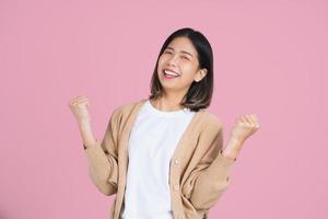 mujer asiática emocionada dama de pie aislado fondo rosa. ella haciendo ganador. foto