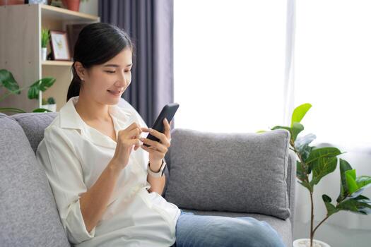 Beautiful Asian woman relaxing on comfortable sofa, enjoying web surfing information in internet or using mobile software application at home. photo