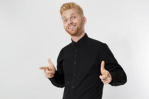 Close up of young guy with redhead and red beard isolated on white background. Stylish man in black shirt pointing copy space. Successful and happy male. Super happy and exciting person. photo