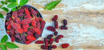 The top view of fresh Mulberrys is a healthy super fruit source of vitamins in a bowl on the old wooden background. mix organic mulberry fruit in Thailand photo