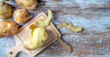 Peeled raw potatoes and raw fresh potatoes on wooden background.top view photo