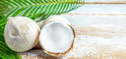 un coco fresco con cáscaras cortadas por la mitad revelando pulpa de coco blanco y hojas de coco sobre un fondo de madera antiguo. foto