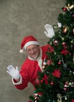 tío santa claus gordo barbudo sonrisa graciosa con sombreros y disfraces agitando saludos durante la decoración del árbol de navidad. feliz navidad feliz año nuevo foto