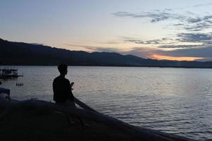 Silhouette of a young man standing by the lake enjoying the sunset. peaceful atmosphere in nature photo