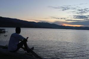Silhouette of a young man standing by the lake enjoying the sunset. peaceful atmosphere in nature photo