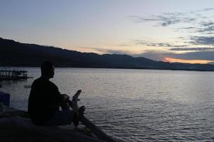 silueta de un joven parado junto al lago disfrutando de la puesta de sol. ambiente tranquilo en la naturaleza foto