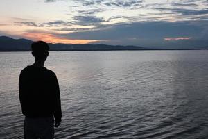 Silhouette of a young man standing by the lake enjoying the sunset. peaceful atmosphere in nature photo