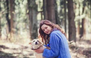 mujer en suéter con perro en el bosque foto