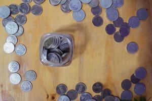 monedas de vista superior planas y vidrio de ahorro en el concepto de ahorro de mesa de madera foto