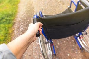 Hand holding empty wheelchair in hospital park waiting for patient services. Wheel chair for person with disability parked outdoor. Accessible for person with disability. Health care medical concept. photo