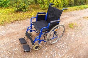 Empty wheelchair standing on road waiting for patient services. Wheel chair for people person with disability parked outdoor. Accessible for person with disability. Health care medical concept. photo