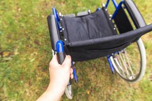 Hand holding empty wheelchair in hospital park waiting for patient services. Wheel chair for person with disability parked outdoor. Accessible for person with disability. Health care medical concept. photo