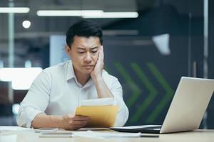 Sad over thinking asian businessman reading bad news letter from bank photo