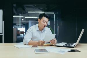 Sad over thinking asian businessman reading bad news letter from bank photo