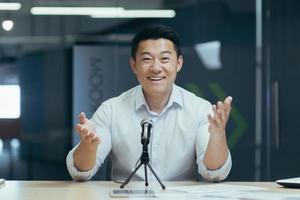 Portrait of a young handsome Asian man speaking to the camera into a microphone photo