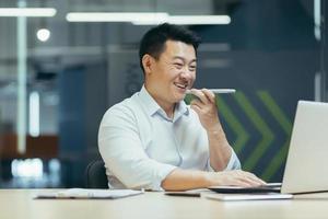 Happy Asian business owner working in modern office typing on laptop photo