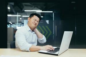 Overtired asian worker in office, having severe neck pain photo