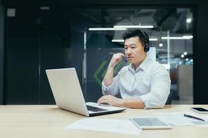 exitoso empresario jefe de empleados asiáticos que trabaja con una computadora portátil usando auriculares