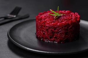 Cooked grated beetroot formed as a cylinder and ready dish on a black plate photo