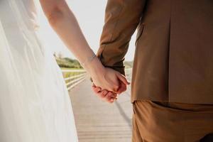 Close up of cute young newlyweds holding their hands against calm sea with lighthouse photo