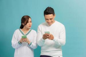 mujer curiosa espiando y mirando el teléfono inteligente de su novio mientras están juntos sobre un fondo claro foto